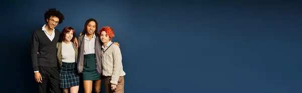 A diverse group of young friends, including a nonbinary individual, stand together in stylish attire on a dark blue background. — Stock Photo