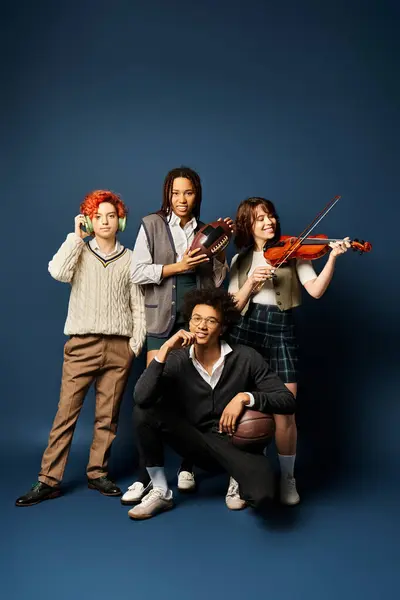 Divers jeunes amis, y compris une personne non binaire, en tenue élégante, se tenant unis avec des instruments de musique sur un fond bleu foncé. — Photo de stock
