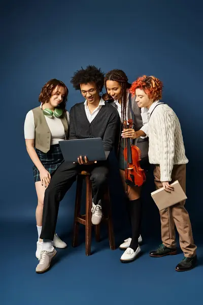 Des amis multiculturels se blottissent autour d'un ordinateur portable en tenue élégante, captivés par l'écran, sur fond bleu foncé. — Photo de stock