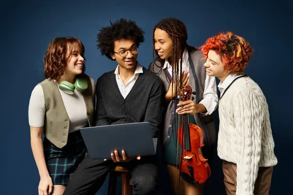 Young multicultural friends, standing together in stylish attire, collaborating around a laptop on a dark blue background. — Stock Photo