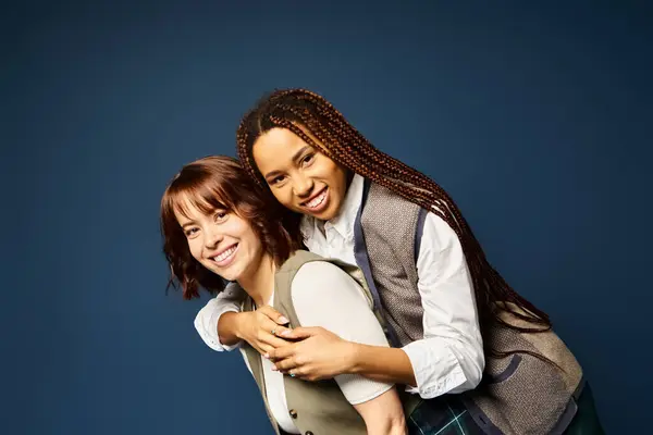 Two young women, hugging joyfully in stylish attire against a dark blue background. — Stock Photo