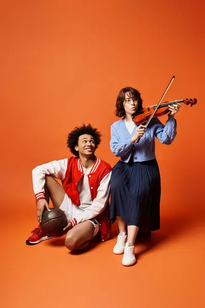 Ein junges multikulturelles Paar, das harmonische Melodien kreiert, während es in stilvoller Kleidung Geige spielt. — Stock Photo