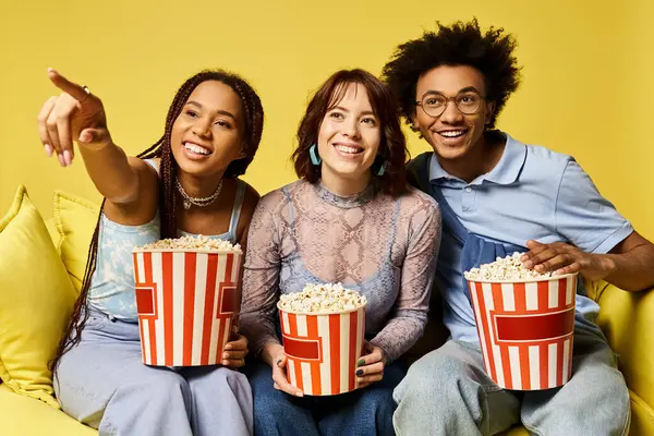 Drei Freunde genießen einen Filmabend auf einer gemütlichen Couch, Popcorn-Eimer in der Hand. — Stockfoto