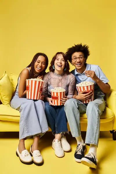 Junge multikulturelle Freunde sitzen auf einer Couch, halten Popcornboxen in der Hand und genießen gemeinsam einen Filmabend in einem stilvollen Studio-Ambiente. — Stockfoto