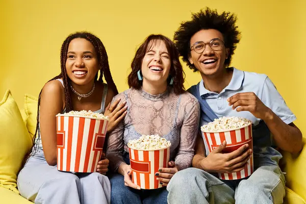 Jóvenes amigos multiculturales sentados en un sofá, sosteniendo palomitas de maíz, disfrutando de una noche de cine juntos. - foto de stock