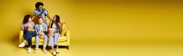 Eine Gruppe junger multikultureller Freunde in stylischer Kleidung sitzt zusammen auf einem gelben Stuhl in einem Studio-Ambiente. — Stockfoto