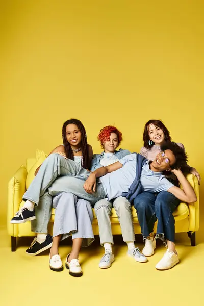 Young multicultural friends in stylish attire sitting on top of a yellow couch, enjoying each others company. — Stock Photo