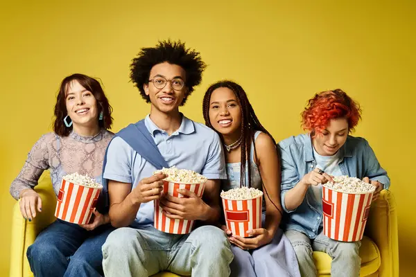 A diverse group of young friends chilling together on a stylish yellow couch in a studio setting. — Stock Photo