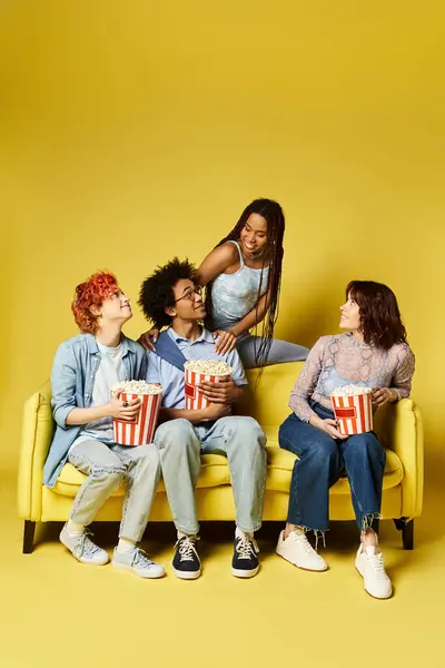 Multicultural group in stylish attire sitting and chatting on a bright yellow couch in a studio setting. — Stock Photo