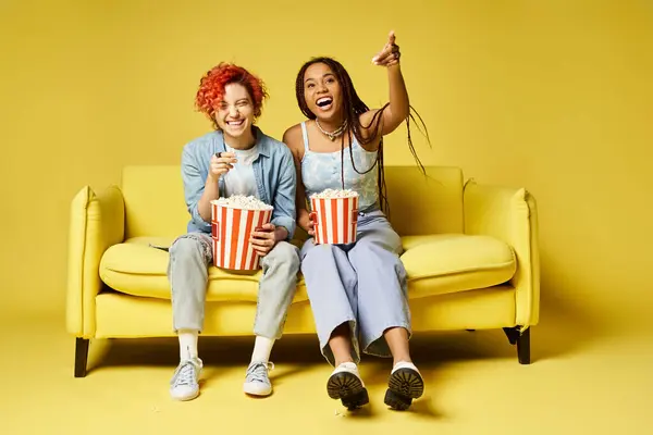 Diverse friends sitting atop a yellow couch and watching movie in a stylish setting. — Stock Photo