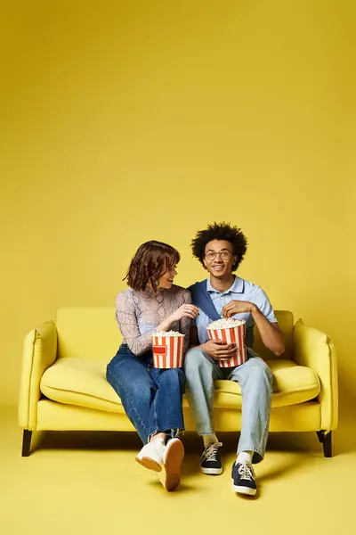 Ein Mann und eine Frau sitzen zusammen auf einer gelben Couch und umarmen sich liebevoll in einem sonnendurchfluteten Raum.. — Stockfoto