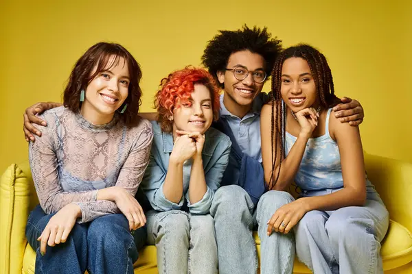 Young multicultural friends in stylish attire relax on a yellow couch in a studio setting. — Stock Photo