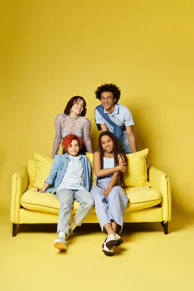 Gli amici multiculturali si rilassano su un divano giallo brillante in un elegante ambiente da studio. — Foto stock