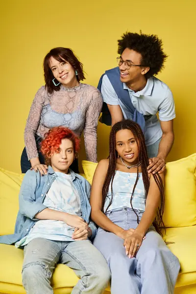 Multikulturelle Freunde in stilvoller Kleidung sitzen auf einer leuchtend gelben Couch in einer gemütlichen Studioatmosphäre und schaffen eine warme und inklusive Atmosphäre. — Stockfoto