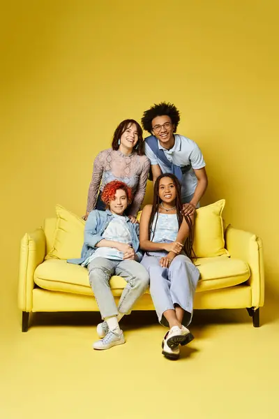 Мультикультурные друзья в стильной одежде смеются и общаются, сидя на ярком желтом диване в студии. — стоковое фото