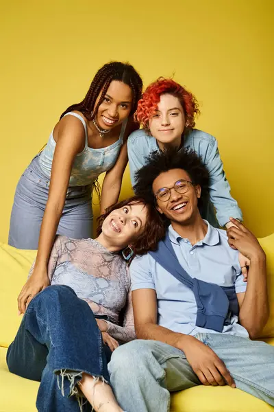 A diverse group of young friends in stylish attire sitting on a vibrant yellow couch in a studio setting. — Stock Photo