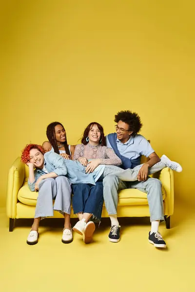 Um grupo diversificado de amigos, incluindo um indivíduo não binário, casualmente sentados em um sofá amarelo brilhante em um estúdio elegante. — Fotografia de Stock