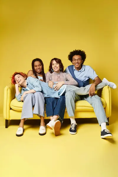 Un groupe diversifié de jeunes amis dans des tenues élégantes se prélassant et bavardant sur un canapé jaune vibrant dans un cadre de studio. — Photo de stock