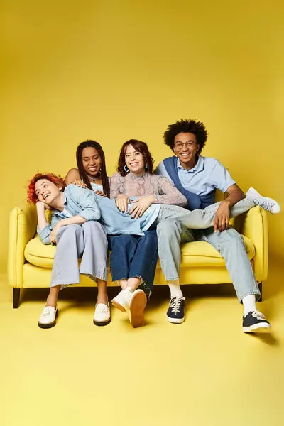 A diverse group of young friends in stylish outfits casually lounging and chatting on a vibrant yellow couch in a studio setting. — Stock Photo