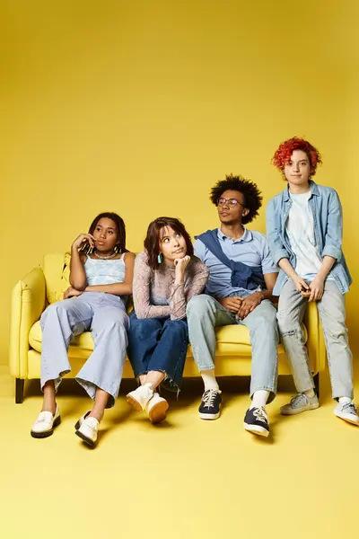 Un groupe de jeunes amis multiculturels s'assoient et rient sur un canapé jaune vif dans un cadre de studio élégant. — Photo de stock