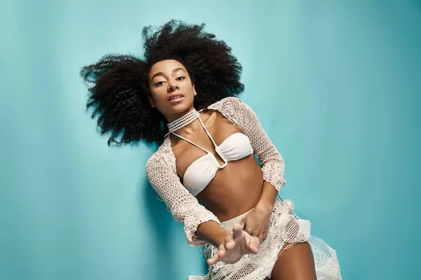 Stunning African American woman in white bikini poses gracefully on vibrant blue background. — Stock Photo