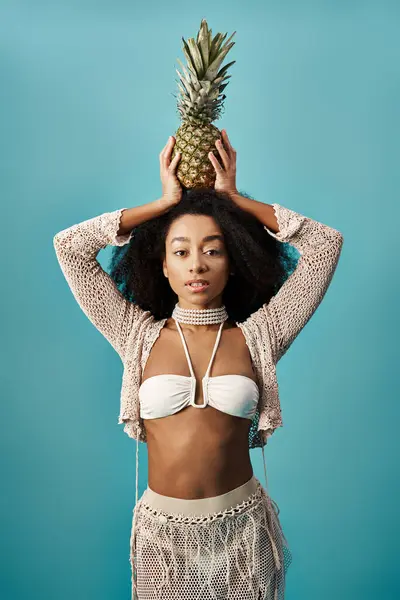 Young African American woman in stylish swimsuit balancing pineapple on head. — Foto stock