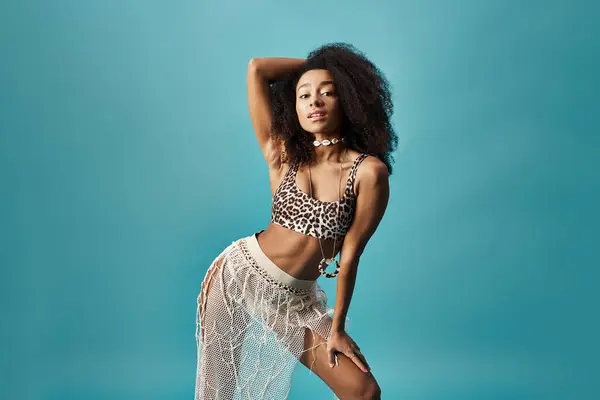 Young African American woman posing in trendy leopard swimsuit on a vibrant blue background. — Stock Photo