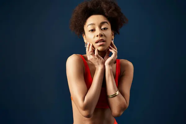 Femme afro-américaine élégante en bikini orange, mains sur le visage, respirant la confiance. — Photo de stock