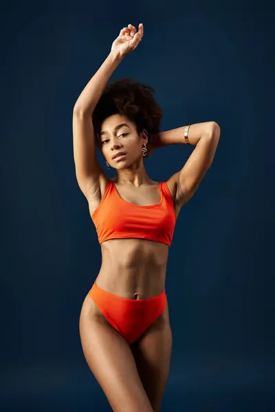 Stilvolle junge Afroamerikanerin posiert im orangefarbenen Bikini vor blauem Hintergrund. — Stockfoto