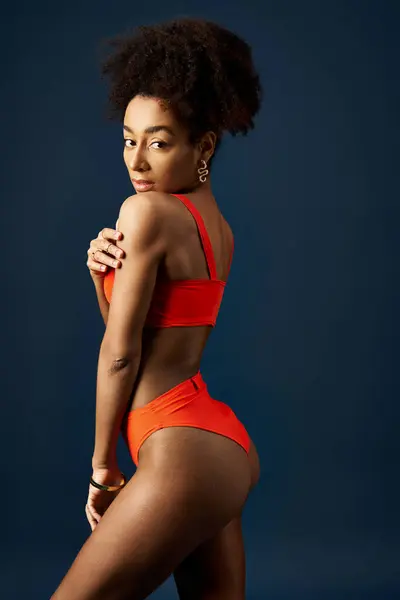Stylish young woman in orange bikini striking pose against bright blue background. — Stock Photo