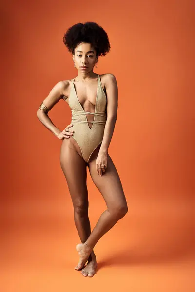 Femme afro-américaine frappant une pose en maillot de bain or sur fond orange. — Photo de stock