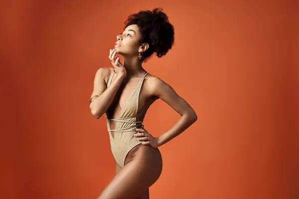 Stylish African American woman in a trendy bikini striking a pose against a bright orange background. — Stock Photo