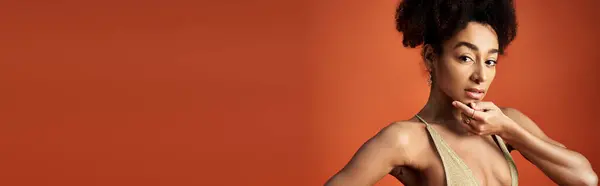 Young African American woman striking a pose in trendy swimsuit against vibrant orange backdrop. — Stock Photo