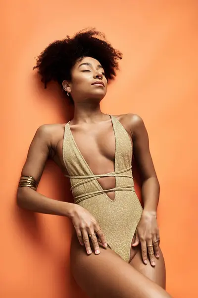 Mulher afro-americana elegante em maiô de ouro golpeia uma pose no fundo laranja vibrante. — Fotografia de Stock