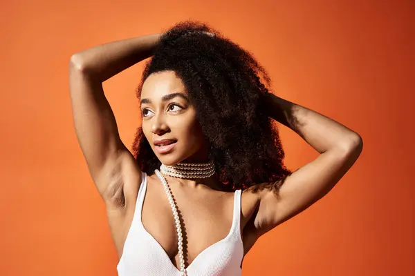 Stylish African American woman in white bikini striking a pose on vibrant orange backdrop. — Stock Photo