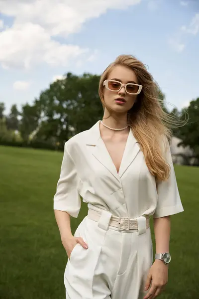 A graceful woman in a white jumpsuit strikes a pose in a lush field, embodying elegance and sophistication. — Stock Photo