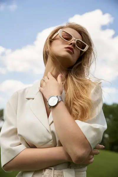 Uma mulher na moda em uma camisa branca elegante e óculos de sol na moda de pé com confiança ao ar livre. — Fotografia de Stock