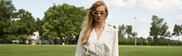 A stylish woman in a white shirt and sunglasses walks gracefully on a grassy field. — Stock Photo