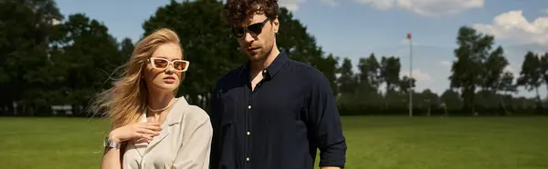 A man and woman in sunglasses, wearing elegant clothing, stand in a lush green field, exuding old-money style and a luxurious lifestyle. — Stock Photo