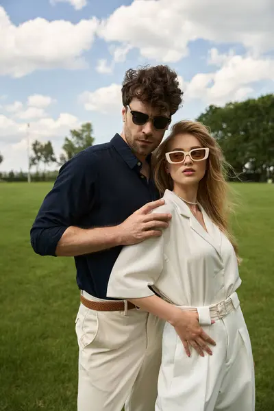 A beautiful young couple, dressed in elegant attire, poses affectionately in a lush green field under the vast sky. — Stock Photo
