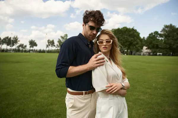 Um homem e uma mulher, elegantemente vestidos, estão juntos em um campo verde exuberante, incorporando uma vida de luxo e sofisticação. — Fotografia de Stock