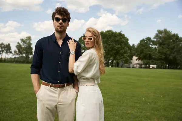 A chic young couple in elegant attire striking poses among lush greenery in a field. — Stock Photo