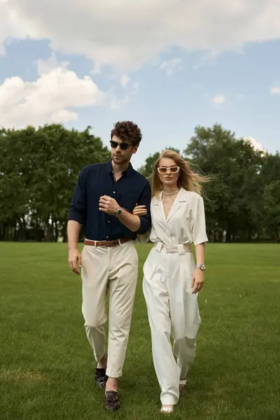 A man and woman in elegant attire enjoy a leisurely walk in a lush, green field. — стокове фото