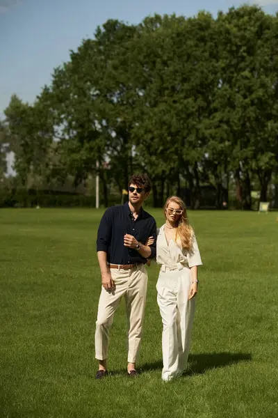 A beautiful young couple in elegant attire stands together in a lush green field, embodying an old-world luxury lifestyle. — Stock Photo