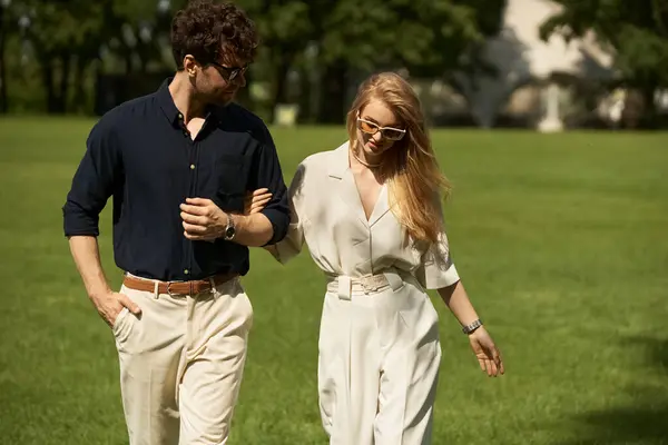A stylish young couple, elegantly dressed, leisurely walk together in a lush park setting. — Stock Photo