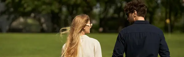 A beautiful young couple in elegant clothing stroll through a green park, exuding old money style and living a rich people lifestyle. — Stock Photo