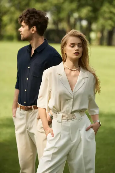 A beautiful young couple in elegant attire stands side by side in a vast grassy field, exuding timeless sophistication. — Stock Photo