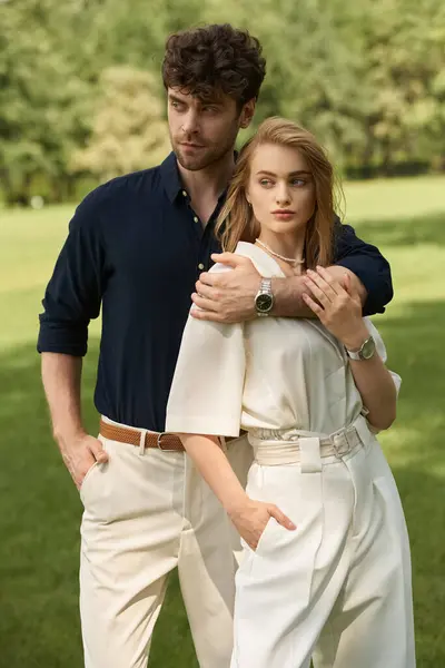 Молода пара одягнена елегантно позують у парк, наповнений яскравою зеленню, демонструючи класичну вишуканість. — стокове фото