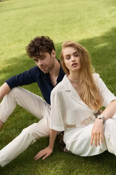 Jovem casal em traje elegante relaxante na grama, incorporando o velho estilo de dinheiro em meio ao campo verde exuberante. — Fotografia de Stock