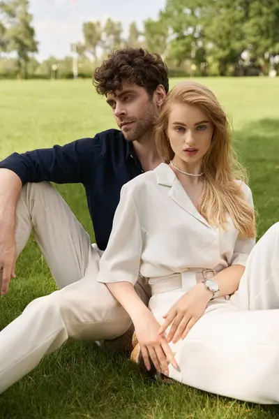 Um jovem casal vestido elegantemente senta-se na grama verde exuberante, incorporando o estilo de dinheiro antigo e um estilo de vida luxuoso. — Fotografia de Stock